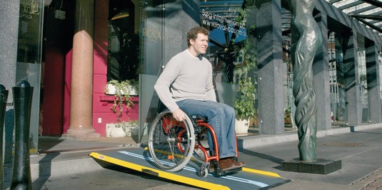 Personne ne fauteuil roulant descendant une rampe d'accès PMR